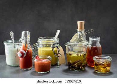 Various condiments in jars and bottles on dark surface with copy space above for concept about food