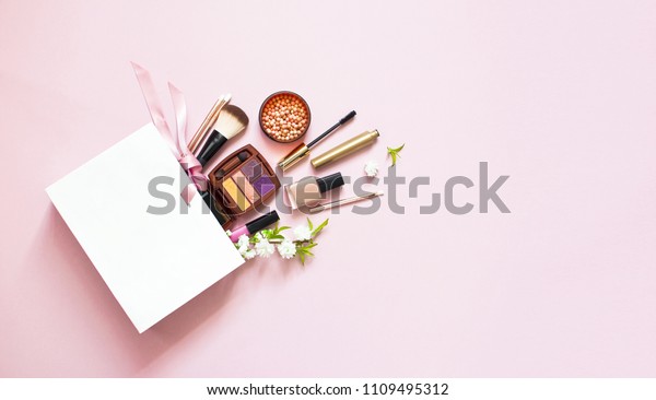 ピンクのパステル背景に白いギフトバックにコピースペースと白いギフトバッグに 化粧品のアイシャドウパウダーリップグロスブラシと白い春の花を塗るマスカラブラシ の写真素材 今すぐ編集