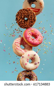 Various decorated doughnuts in motion falling on blue background. Sweet and colourful doughnuts falling or flying in motion.