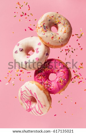 Various decorated doughnuts in motion falling on pink background. Sweet and colourful doughnuts falling or flying in motion.