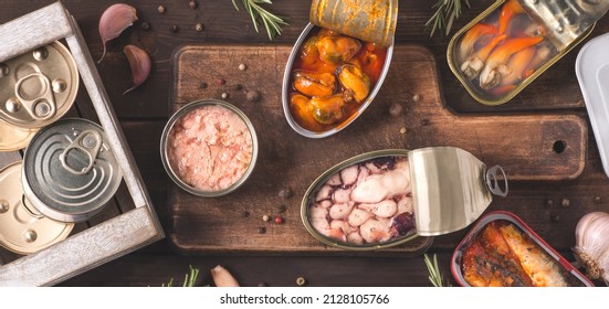 Various Delicious Canned Fish And Seafood In Aluminum Cans On The Dark Wooden Background. Fast Healthy Food, Full Of Omega 3 And Micro Elements.  Top View, Internet Banner