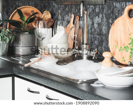 Various dishes - plates, wine glasses, bowls in soapy foam on the sink in the kitchen. Front view