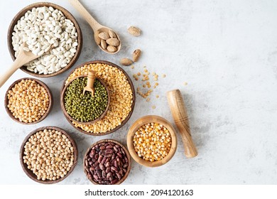 Various dried legumes in wooden bowls top view flat lay on white marble background with copy space
