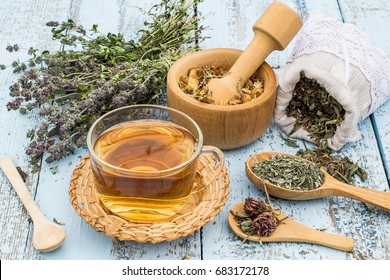 Various dried meadow herbs and herbal tea on light old wooden table. Dried medicinal plants in bag, basket, mortar and in bundle. Preparing medicinal plants for phytotherapy and health promotion