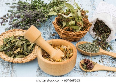 Various dried meadow herbs on light old wooden table. Dried medicinal plants in bag, basket, mortar and in bundle. Preparing medicinal plants for phytotherapy and health promotion