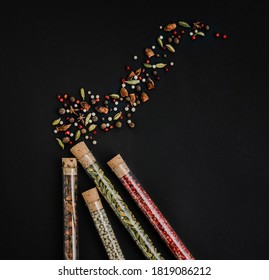 Various Dry Spices In Glass Test Tubes And Pattern On Black Background. Top View. Copy Space.