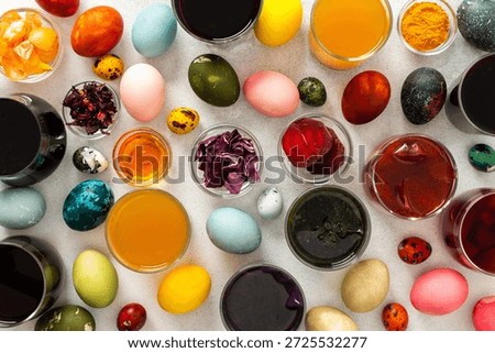 Various dyed Easter eggs in different colors are surrounded by bowls of natural dyes, such as beets, turmeric and flower extracts hibiscus, red cabbage and onion peel, showcasing a creative activity