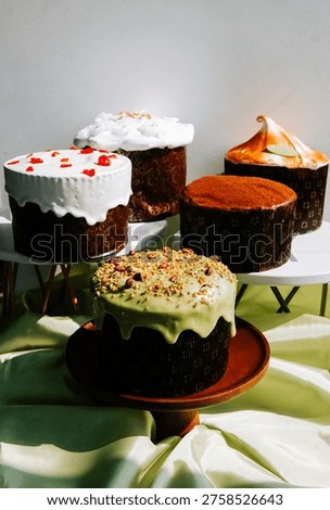 Various Easter cakes sit on cake stands during a holiday celebration in a bright room. The cakes have different toppings and frosting.