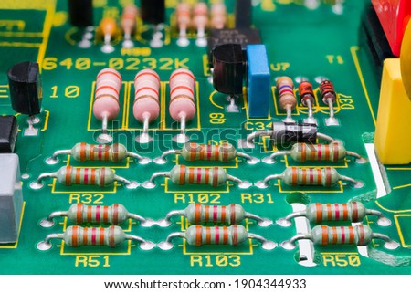Various electronic components on detail of printed circuit board. Electrotechnics. Close-up of resistors with standard color code and transistors or diodes on green PCB with safety air gaps. E-waste.