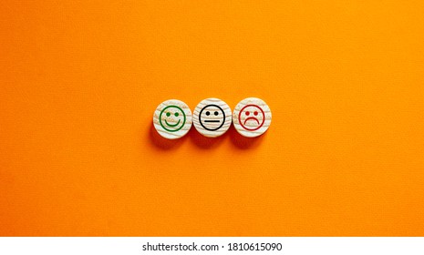 Various emoticons made of wooden circles drawn lines of a mouth. Over orange background in a conceptual image of quality and feedback.