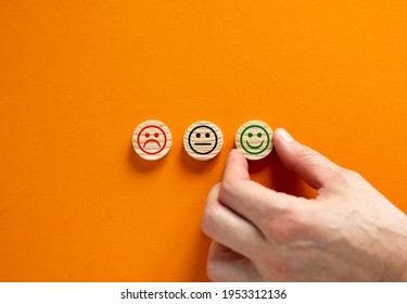 Various Emoticons Made Of Wooden Circles Drawn Lines Of A Mouth. Over Orange Background In A Conceptual Image Of Quality And Feedback. Customer Hand. Business And Feedback Concept.