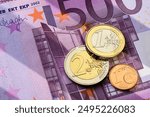 Various euro coins, including one euro, two euro, and one cent, are positioned atop 500 euro banknote.