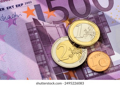 Various euro coins, including one euro, two euro, and one cent, are positioned atop 500 euro banknote.