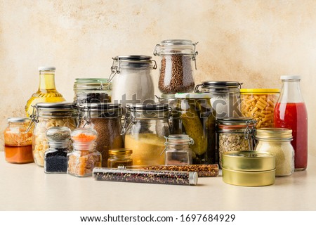 Various food supplies including grains, condiments, tomato sauce, oil in glass bottles and jars, dry pasta, canned produce on kitchen table. Sustainability concept. Horizontal orientation
