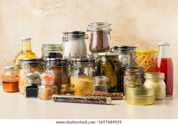 Various\
food supplies including grains, condiments, tomato sauce, oil in\
glass bottles and jars, dry pasta, canned produce on kitchen table.\
Sustainability concept. Horizontal\
orientation