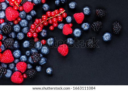 Various fresh forest berries on black stone background, top view. Berry mix. Flat lay. Copyspace