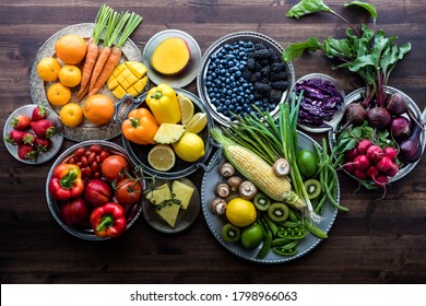 Various fresh organic fruits and vegetables on metal plates in rainbow colours against a dark wooden background. - Powered by Shutterstock