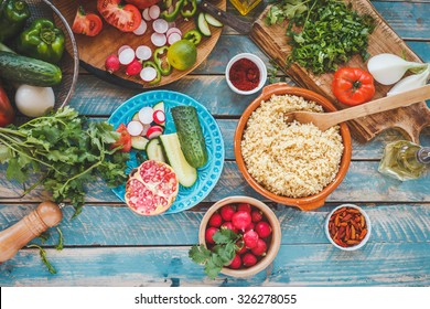 Various Fresh Vegetables On A Blue Wooden Table  And Cook Burghul In Ceramic Bowl Ready To Prepare Arabian Traditional Food. Country Food Concept From Above. Series.