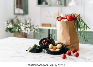 Various Fresh Vegetables In Paper Grocery And Black Mesh Bags On Kitchen Island With Marble Top, Healthy Food Full Of Nutrients, Vintage Furniture With Flowers, Blurred Background