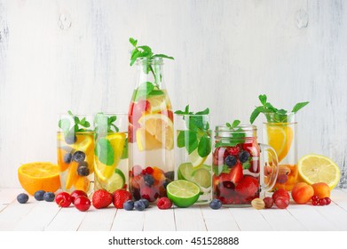 Various fresh vitamin flavored fruit infused water and fruits on white rustic wooden background.