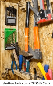 Various hand tools such as hammers, pliers, and drill bits are neatly arranged on a wooden wall in a workshop or garage environment