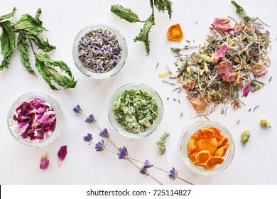 various herbal tea ingredients in glass jars over white wooden background