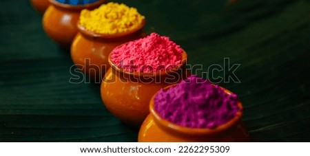 Various Holi paints in pots on a large green palm leaf. Colorful background for the national Indian holiday Happy Holi with copy space.