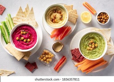 Various hummus dips in bowls, served with fresh vegetables and crisps. Traditional hummus, beetroot hummus and avocado hummus. vegetarian party food concept. top view. - Powered by Shutterstock