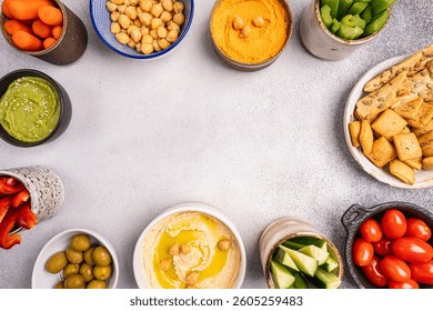 Various hummus dips. Hummus plate with vegetable snacks. Carrot, cucumber, tomato, celery sticks, dry crackers and olive, top view. Vegan and traditional hummus as healthy and vegan snack.