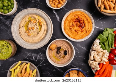 Various hummus dips. Hummus plate with vegetable snacks. Carrot, cucumber, tomato, celery sticks, dry crackers and olive, top view. Vegan and traditional hummus as healthy and vegan snack.