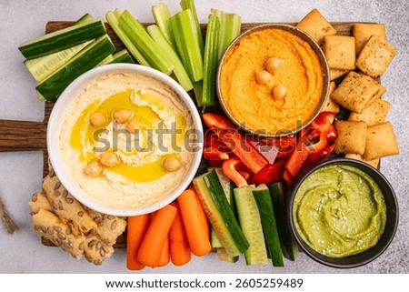 Various hummus dips. Hummus plate with vegetable snacks. Carrot, cucumber, tomato, celery sticks, dry crackers and olive, top view. Vegan and traditional hummus as healthy and vegan snack.