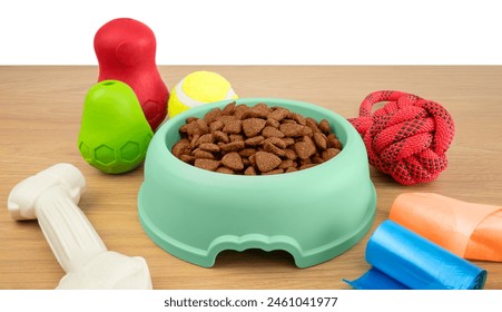 Various items for the dog: a green bowl with food, a red toy, rubber toys, a tennis ball, poopbags, a bone lying on a wooden table. Life with a dog - Powered by Shutterstock