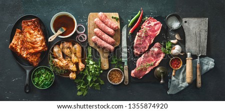 Various kinds of grill and bbq meats with vintage kitchen and butcher utensils. Chicken legs, steaks, sausages, pork ribs with herbs, spices, sauces and ingredients for grilling Stock fotó © 