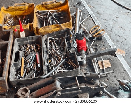 Various mechanical tools, wrenches, screwdrivers, and oil cans in plastic containers at a traditional roadside motorcycle repair shop (tambal ban) in Jakarta, Indonesia.
