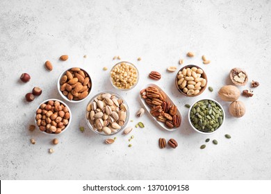Various Nuts in  bowls on white background, top view, copy space. Nuts assortment - pecans, hazelnuts, walnuts, pistachios, almonds, pine nuts, peanuts, pumpkin seeds. - Shutterstock ID 1370109158