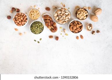 Various Nuts in  bowls on white background, top view, copy space. Nuts assortment frame - pecans, hazelnuts, walnuts, pistachios, almonds, pine nuts, peanuts, pumpkin seeds. - Shutterstock ID 1390152806