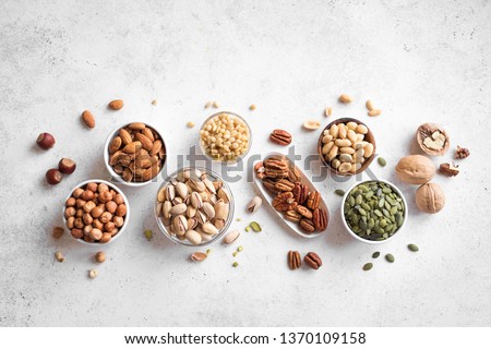 Various Nuts in  bowls on white background, top view, copy space. Nuts assortment - pecans, hazelnuts, walnuts, pistachios, almonds, pine nuts, peanuts, pumpkin seeds.