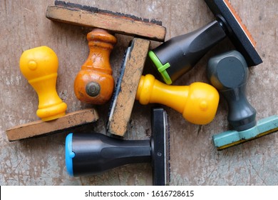 Various Old, Used Rubber Stamps Lying On A Worn Out Table. Closeup, Top View. Name, Title, Designation, Company Seal Rubber Stampers On Old Desk.