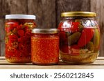 various pickled chilies in preserving jars, preserving chili peppers after harvest, sliced chilies, whole pickled jalapenos and homemade chili paste in preservation jars on a wooden background