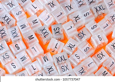 Various plastic clothing size tags, plastic size labels for hangers of clothing store with indexes of the XXS, XS, S, M, L, XL, XXL sizes on a orange background. Close up.