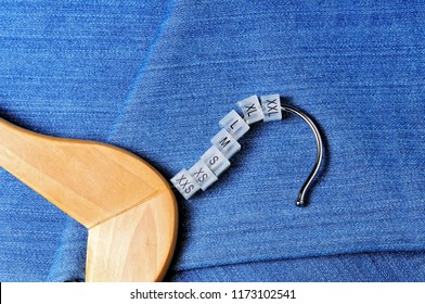 Various plastic clothing size tags, plastic size labels for hangers of clothing store with indexes of the XXS, XS, S, M, L, XL, XXL sizes on a hanger on jeans background.