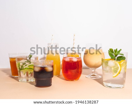 Various refreshing non-alcoholic drinks in glasses with ice. Different juice, homemade lemonade, iced coffee, iced fruit tea and smoothies on beige background. Copy space. Front view