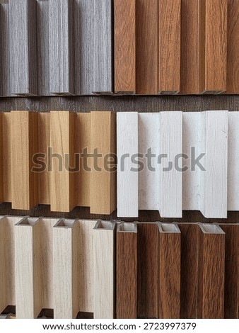 Various samples of fluted wall panels are displayed in a grid pattern to show different wood grain textures and colors. These decorative building materials, including shades of oak, walnut, white, and grey, are presented in a showroom to help clients choose interior wall cladding. The vertical slats create a modern 3D aesthetic for architectural decoration, captured in a close-up shot that emphasizes the material quality and finish.