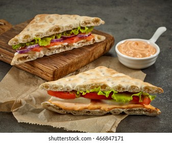 various sandwiches and bowl of sauce on paper and wooden cutting board