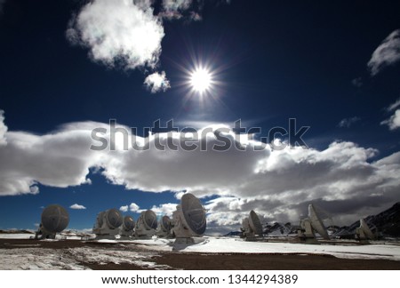 various satellite dishes on the Atacama Large Millimeter Submillimeter Array of ALMA on snow-covered ground under white blue sky