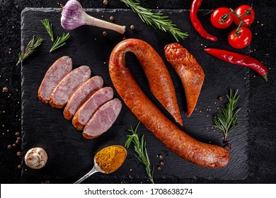 Various Sausages And Smoked Products Lie On A Black Board, Sausage, Sausages, Ribs, Rolls. Top View, Overhead. Flat Lay