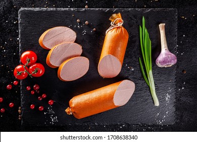 Various Sausages And Smoked Products Lie On A Black Board, Sausage, Sausages, Ribs, Rolls. Top View, Overhead. Flat Lay