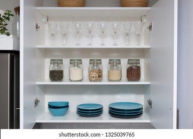 Various Seeds In Storage Jars In Pantry, White Modern Kitchen In Background. Smart Kitchen Organization