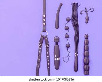 Various sex toys (leather harness, vibrator, whip, dildo, anal balls and other) are on a purple background. The image is suitable for advertising a sex shop.