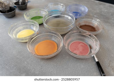 Various shades of paint are neatly arranged in glass bowls on a workspace. - Powered by Shutterstock